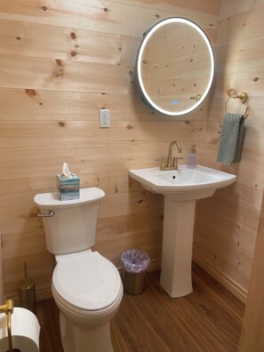 Een badkamer met toilet, wastafel en een ronde spiegel met verlichting.
