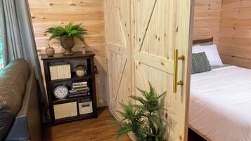 A wooden room with a bed, a small table with a clock, and a potted plant.