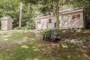 Une cabane avec deux annexes attenantes, un petit abri de jardin et un banc situés dans une zone boisée.