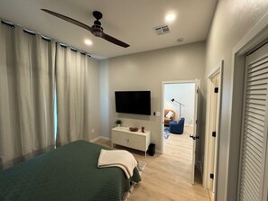 Una camera da letto con un letto, una ventola a soffitto, una TV, una cassettiera e una porta che conduce a un'altra stanza.