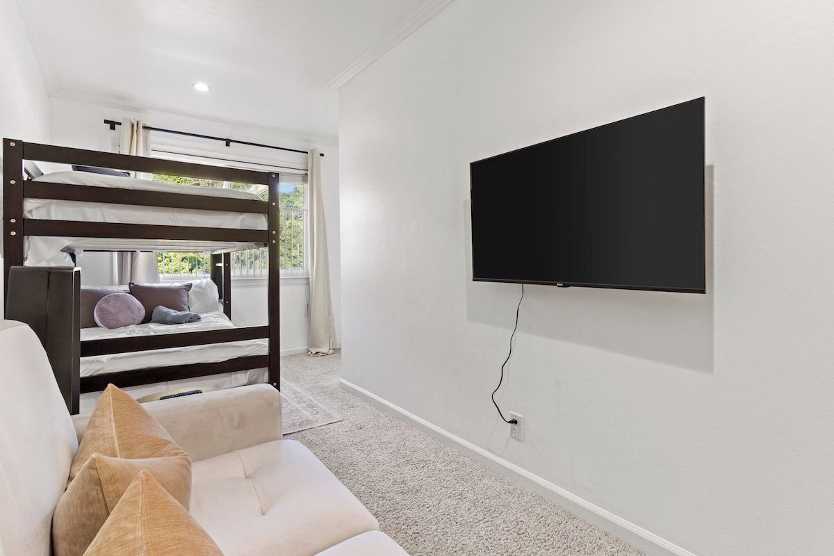 A room with a bunk bed, a sofa, and a mounted TV.
