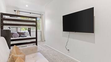 A room with a bunk bed, a sofa, and a mounted TV.