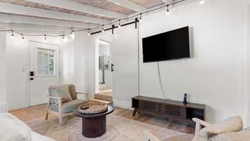 Un salon moderne avec un téléviseur à écran plat, un parquet, une table basse ronde et un canapé.