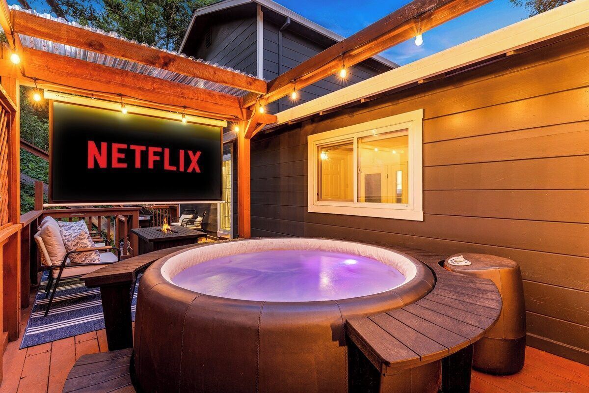 Uma banheira de hidromassagem com deck de madeira, sinal da Netflix e uma janela com cortinas.
