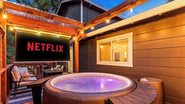 Ein Whirlpool mit Holzterrasse, einem Netflix-Schild und einem fensterbepflanzten Fenster.