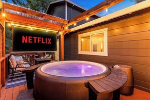 Una banyera d'hidromassatge amb un pont de fusta, un cartell de Netflix i una finestra amb cortines.