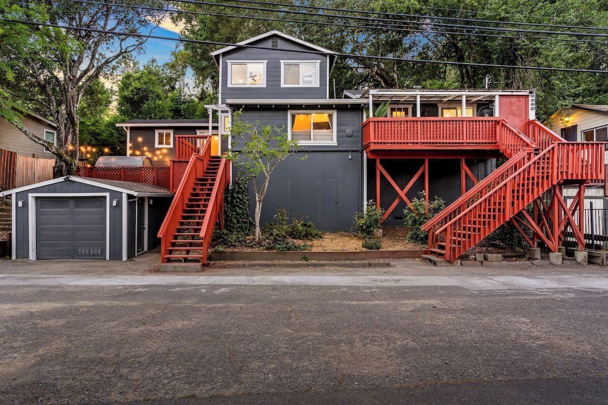 Uma casa de dois andares com uma escadaria vermelha, garagem e um pequeno jardim.