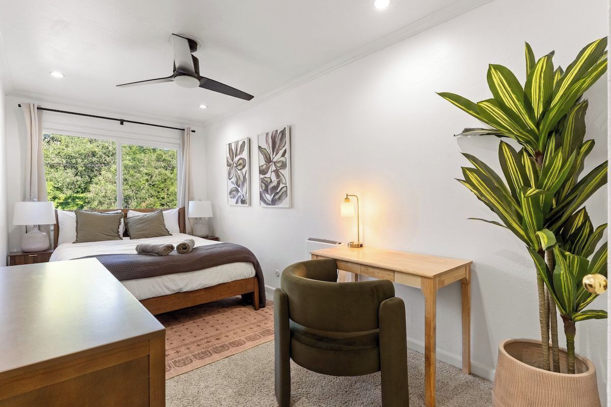 Quarto com cama, escrivaninha, cadeira e uma grande planta em vaso.