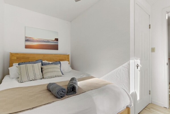 A bedroom with a bed, pillows, a blanket, and a painting on the wall.