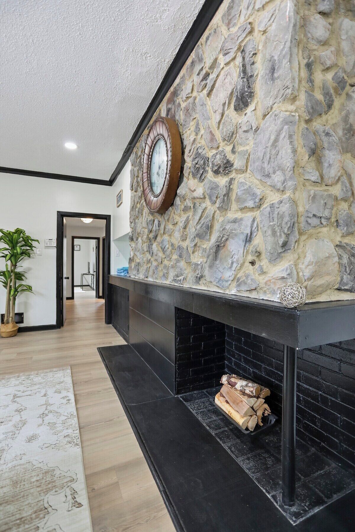 A modern interior with a stone wall, a fireplace with logs, and a clock.
