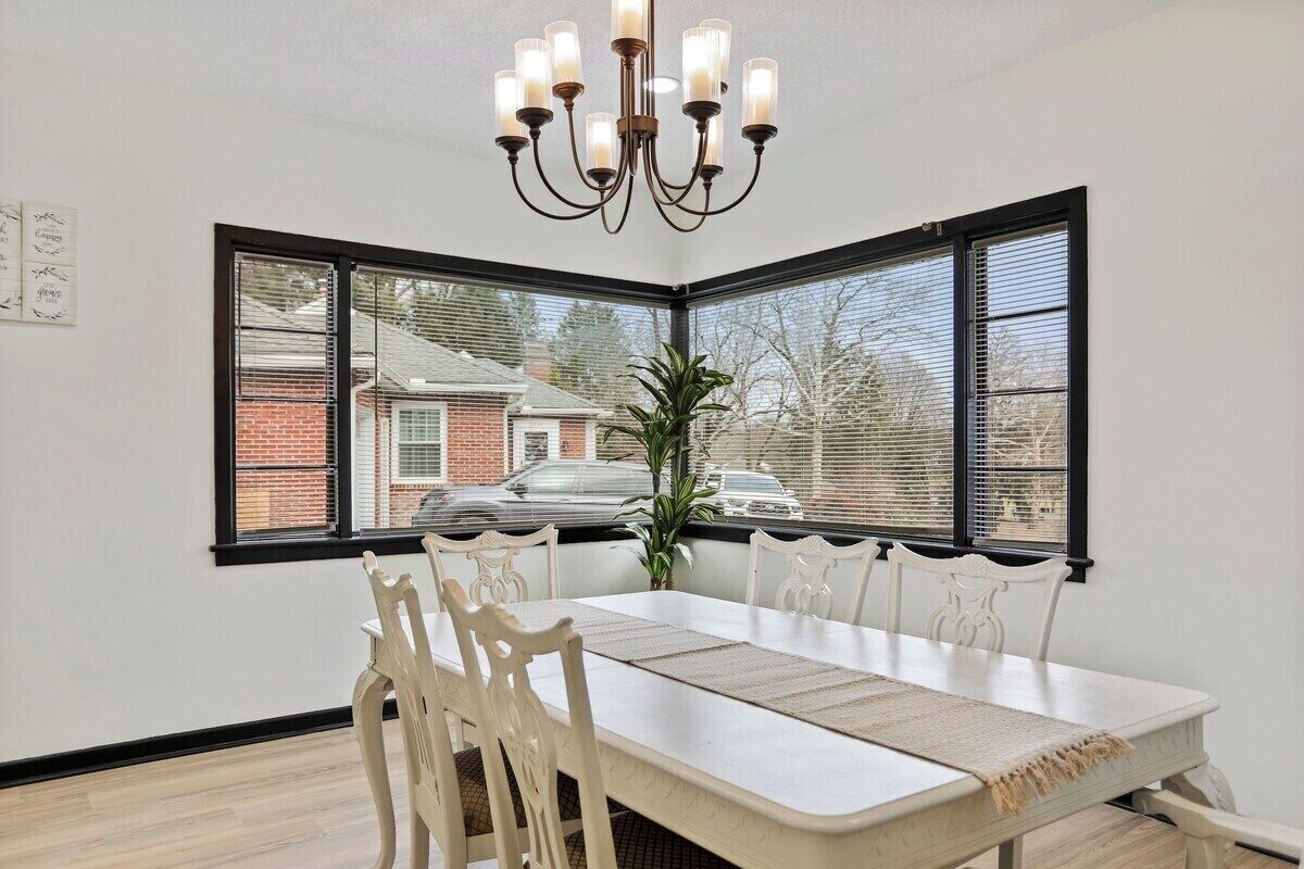 A dining area with a white table, matching chairs, a chandelier, and a view through large windows.