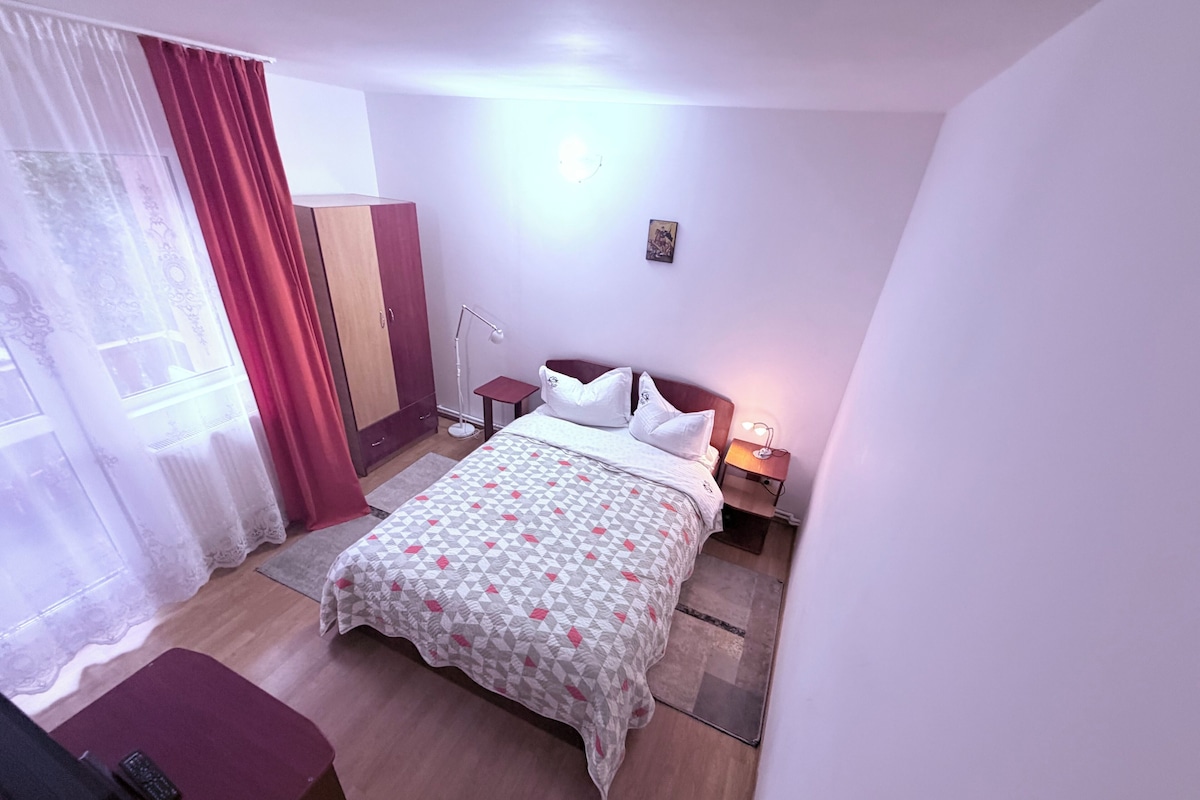 Una habitación de hotel con una cama, mesitas de noche, un escritorio, un armario y una ventana con cortinas.