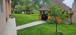 Una cabaña de troncos con un porche, un pequeño jardín y un sendero pavimentado que lleva a la entrada.