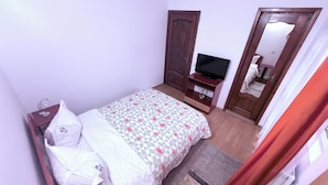 A bedroom with a bed, a television on a stand, a wardrobe, and a mirror.