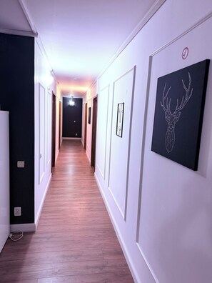 A hallway with wooden flooring, white walls, and framed artwork.