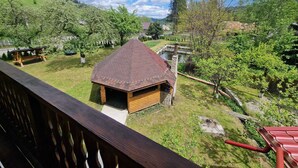 A wooden cabin with a thatched roof, surrounded by a lush green landscape and a clear blue sky.