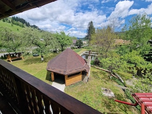 A wooden cabin with a thatched roof, surrounded by a lush green landscape and a clear blue sky. - Villa Ileana  (Ceahlău)