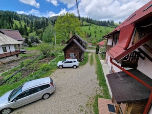 A rural setting with a gravel driveway, a white car parked in the driveway, and a wooden cabin with a red roof.