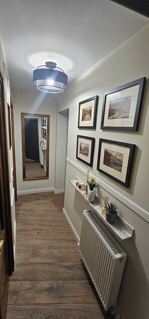 A hallway with a radiator, framed pictures on the wall, a mirror, and a hanging light fixture. - Villa Ileana  (Ceahlău)