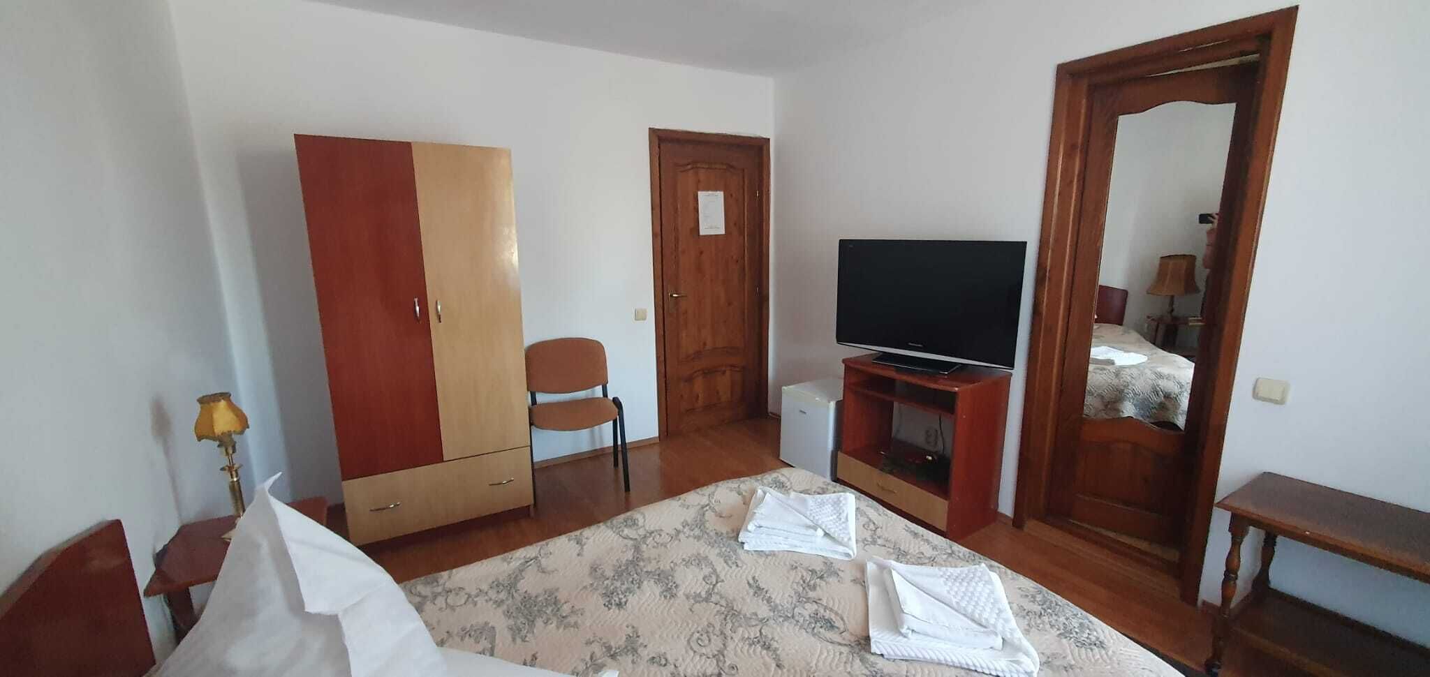 Quarto com cama, guarda-roupa, televisão, cadeira e espelho.