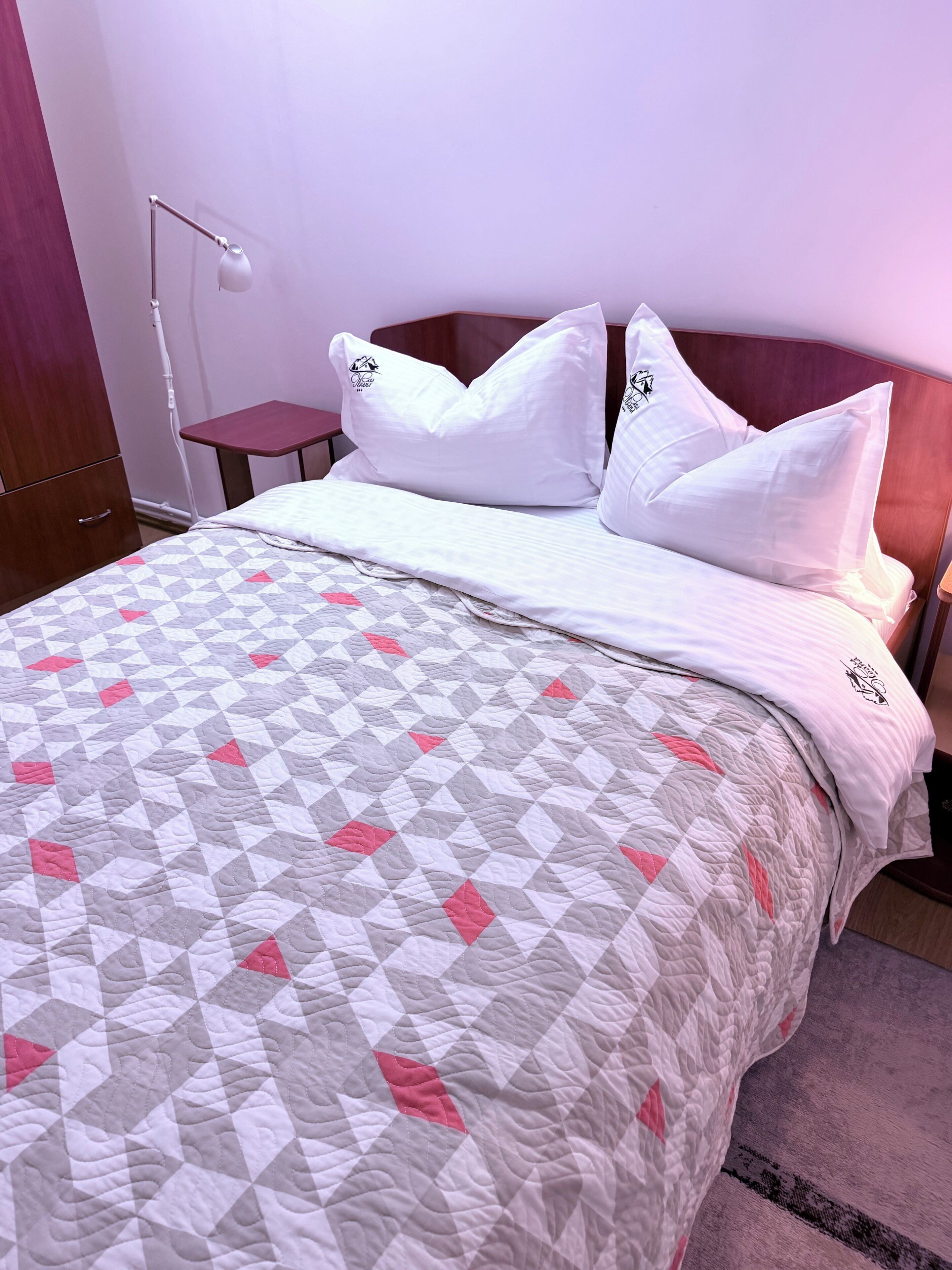 Una habitación de hotel con una cama, almohadas, una mesita de noche y una lámpara.