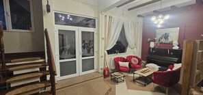 A living room with a piano, red chairs, a wooden staircase, and a window with curtains. - Villa Ileana  (Ceahlău)