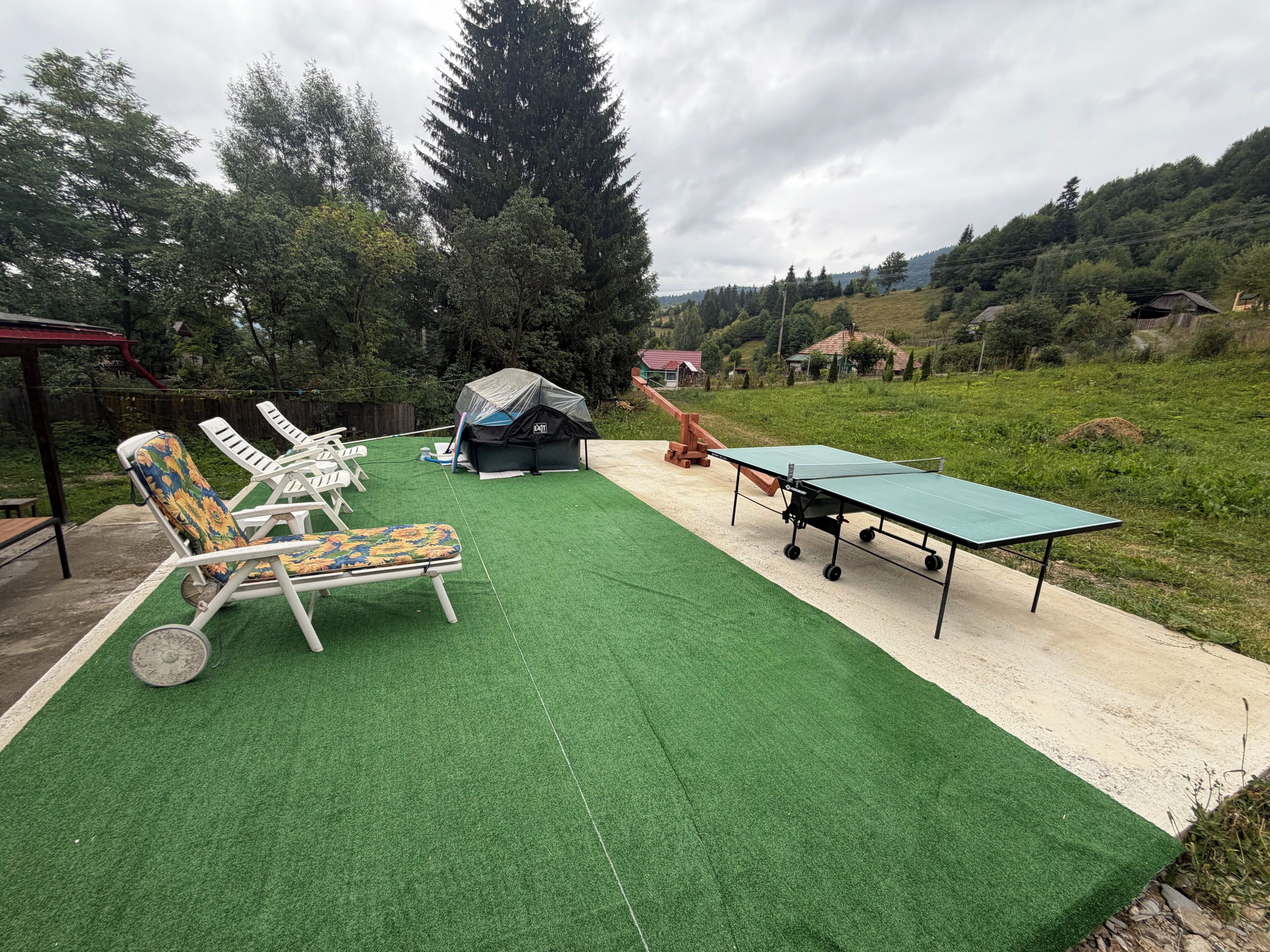An outdoor area with artificial turf, a ping pong table, and lounge chairs.