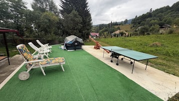 An outdoor area with artificial turf, a ping pong table, and lounge chairs.