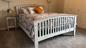 A white metal bed with a headboard, a bedside table with a lamp, and a wall-mounted light fixture.