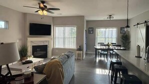 A living room with a sofa, a TV, a fireplace, and a dining area with a table and chairs. - 3bed 2 bath with King master Sycamore (Sycamore)