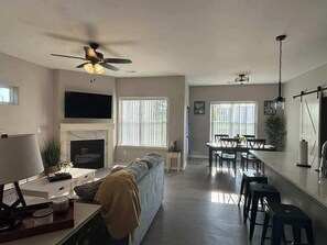 A living room with a sofa, a TV, a fireplace, and a dining area with a table and chairs. - 3bed 2 bath with King master Sycamore (Sycamore)