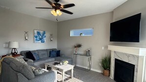 A living room with a gray sofa, a coffee table, a fireplace, and a ceiling fan.