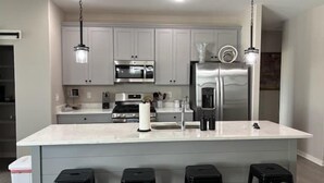 A modern kitchen with a large island, stainless steel appliances, and black bar stools. - 3bed 2 bath with King master Sycamore (Sycamore)
