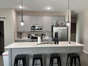 A modern kitchen with a large island, stainless steel appliances, and black bar stools. - 3bed 2 bath with King master Sycamore (Sycamore)