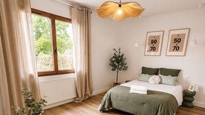 Un dormitori amb un llit, una taula rodona amb una planta, una finestra amb cortines i obra d'art amb marc a la paret.