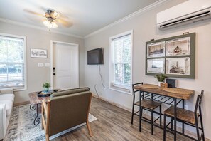 A room with a ceiling fan, a flat-screen TV mounted on the wall, a dining table with chairs, and a window with blinds. - Coastal charm awaits in this cozy 1-bed, 1-bath home on Fairhope’s Scenic Hwy 98 (Fairhope)