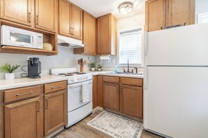 A kitchen with wooden cabinets, a white stove, a microwave, a coffee maker, and a refrigerator. - Coastal charm awaits in this cozy 1-bed, 1-bath home on Fairhope’s Scenic Hwy 98 (Fairhope)