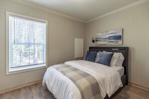 A bedroom with a bed, a window with blinds, a painting on the wall, and a door. - Coastal charm awaits in this cozy 1-bed, 1-bath home on Fairhope’s Scenic Hwy 98 (Fairhope)