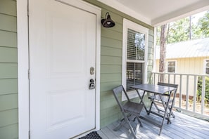 A white front door with a keyhole and a doorbell, a small table with chairs, and a window with blinds. - Coastal charm awaits in this cozy 1-bed, 1-bath home on Fairhope’s Scenic Hwy 98 (Fairhope)