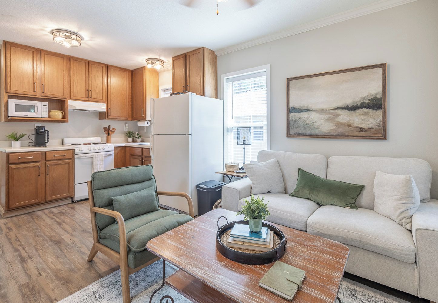A modern kitchen with wooden cabinets, a white refrigerator, and a dining area with a green chair and a wooden table.