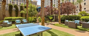 Un espace de loisirs en plein air comprenant une table de ping-pong, des meubles en osier et un jardin bien entretenu avec des palmiers et des arbustes.