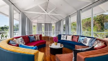 Ein geräumiger Raum mit einer gebogenen Eckcouch, einem runden Couchtisch und Blick auf Grün durch große Fenster.