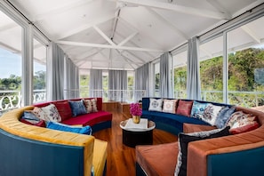 A spacious room with a curved sectional sofa, a round coffee table, and a view of greenery through large windows.