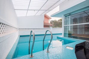 Ein Innenpool mit zwei Metallleitern, einem gefliesten Boden und einer Glaswand mit Blick ins Freie.