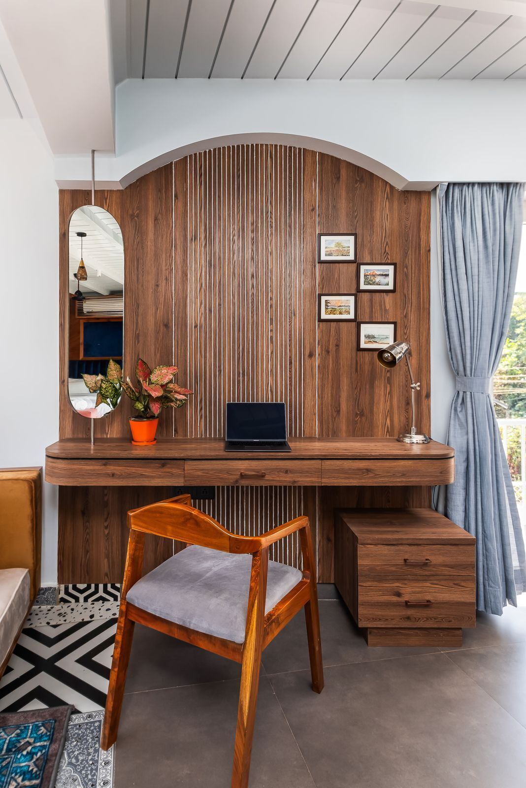 Un espace de travail moderne avec un bureau en bois, un ordinateur portable et une chaise. Des tableaux encadrés ornent le mur et une plante en pot est posée sur le bureau.