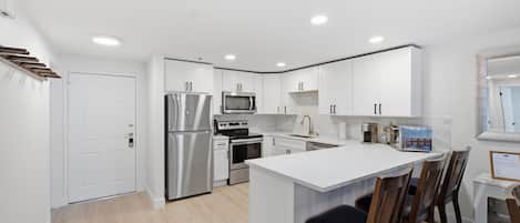 A modern kitchen with white cabinetry, stainless steel appliances, and a central island with bar stools.