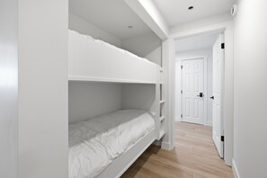 Un lit superposé avec un matelas blanc et un lit inférieur également doté d’un matelas blanc. On aperçoit une porte blanche à l’arrière-plan.