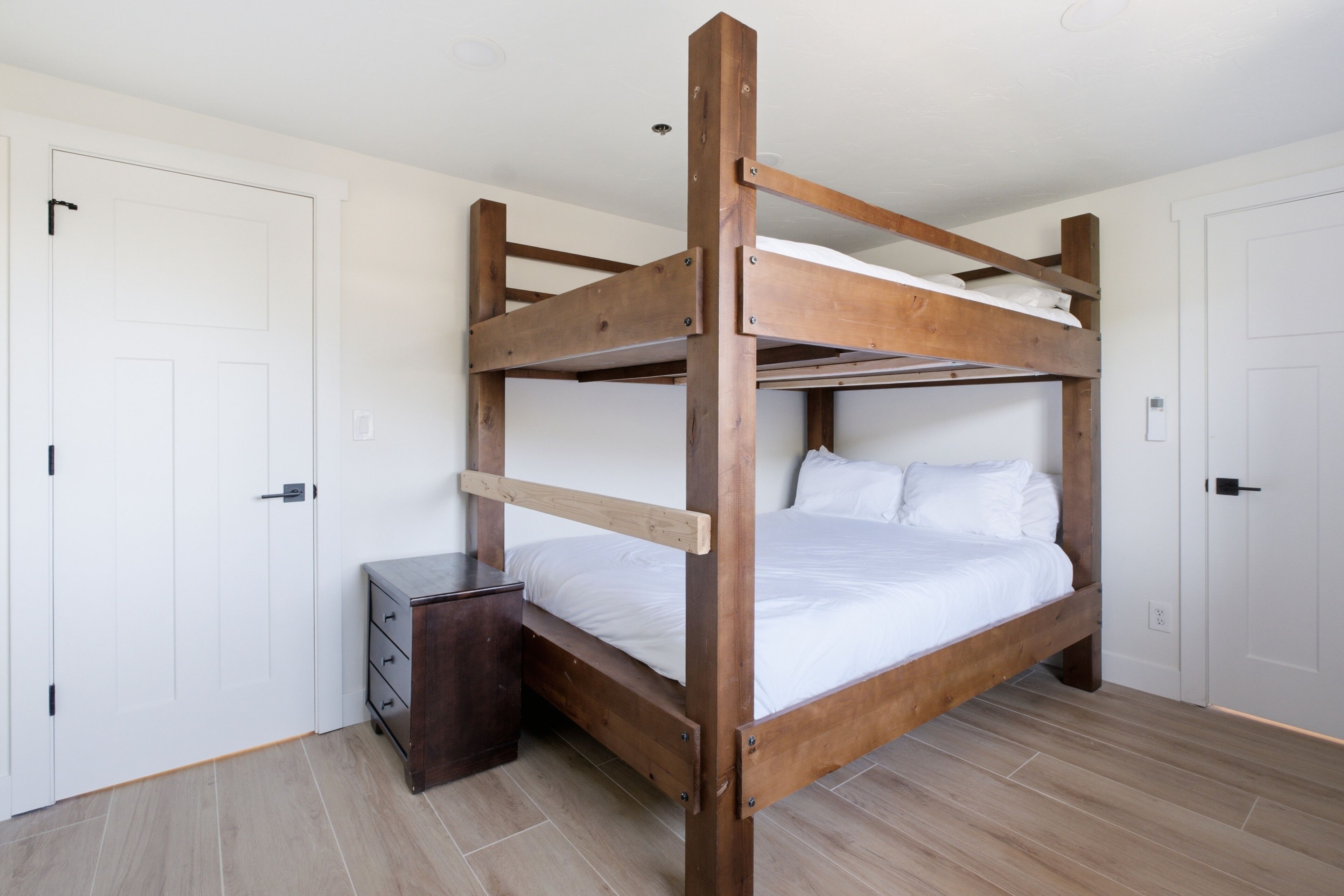 Ein Stockbett mit Holzrahmen, weißer Bettwäsche und einer kleinen Holzkommode.