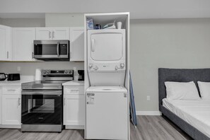 A compact kitchenette with a microwave, stove, oven, and a white washing machine. - The Onyx Studio • DT Oshawa (Oshawa)