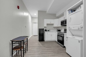 Une cuisine moderne avec des meubles blancs, un réfrigérateur noir, un four à micro-ondes, un four traditionnel et un lave-linge.